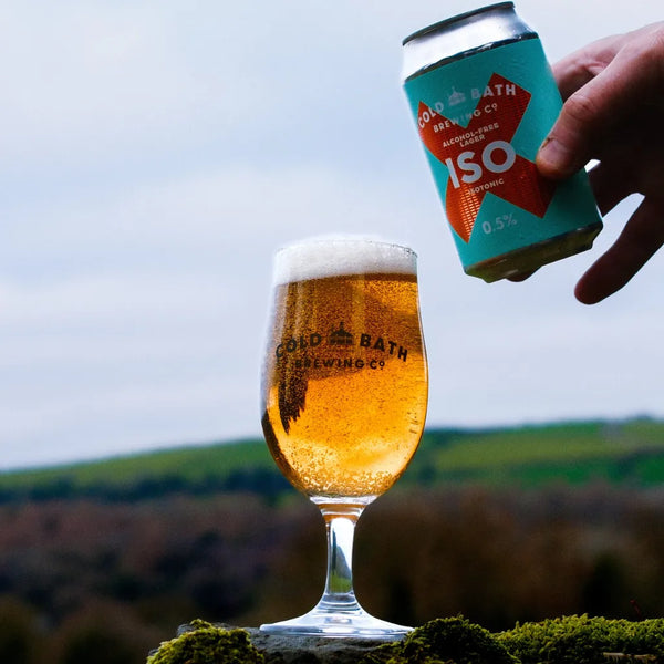 Cold Bath ISO alcohol free isotonic lager poured into a branded glass, with the can held above